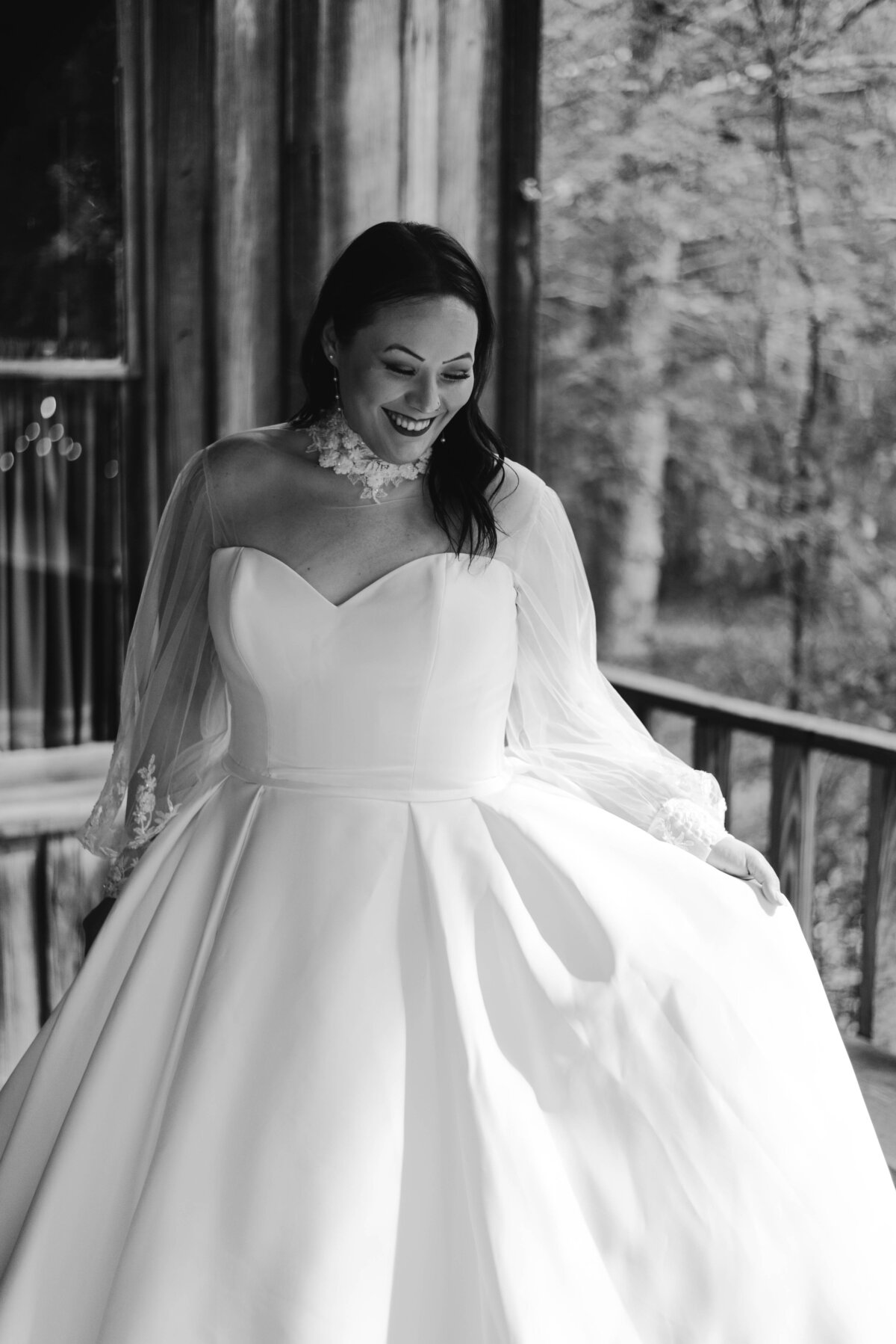 a black and white photo of a bride fanning out her white wedding dress while smiling.
