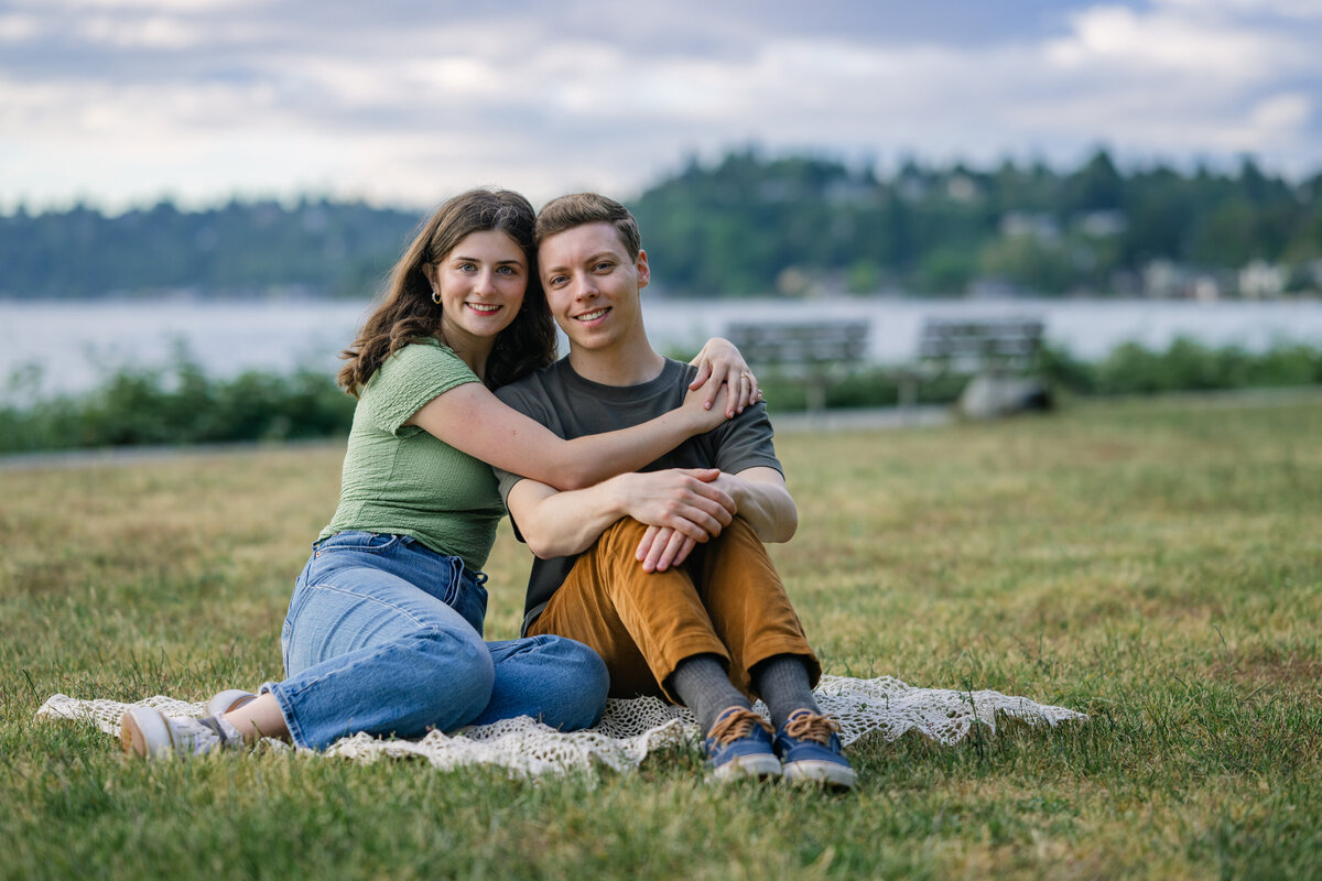 engaged man and woman sit on grass at lincoln park seattle