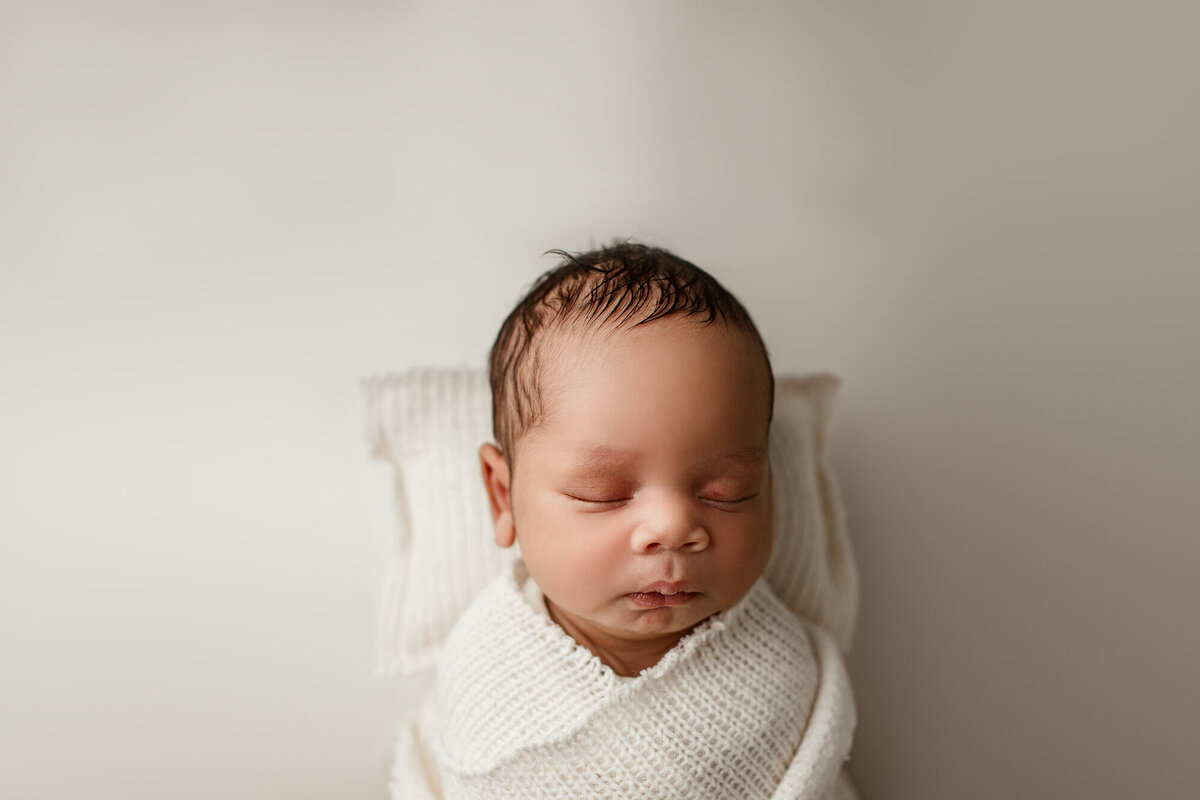 baby swaddled posed on soft cream pillow
