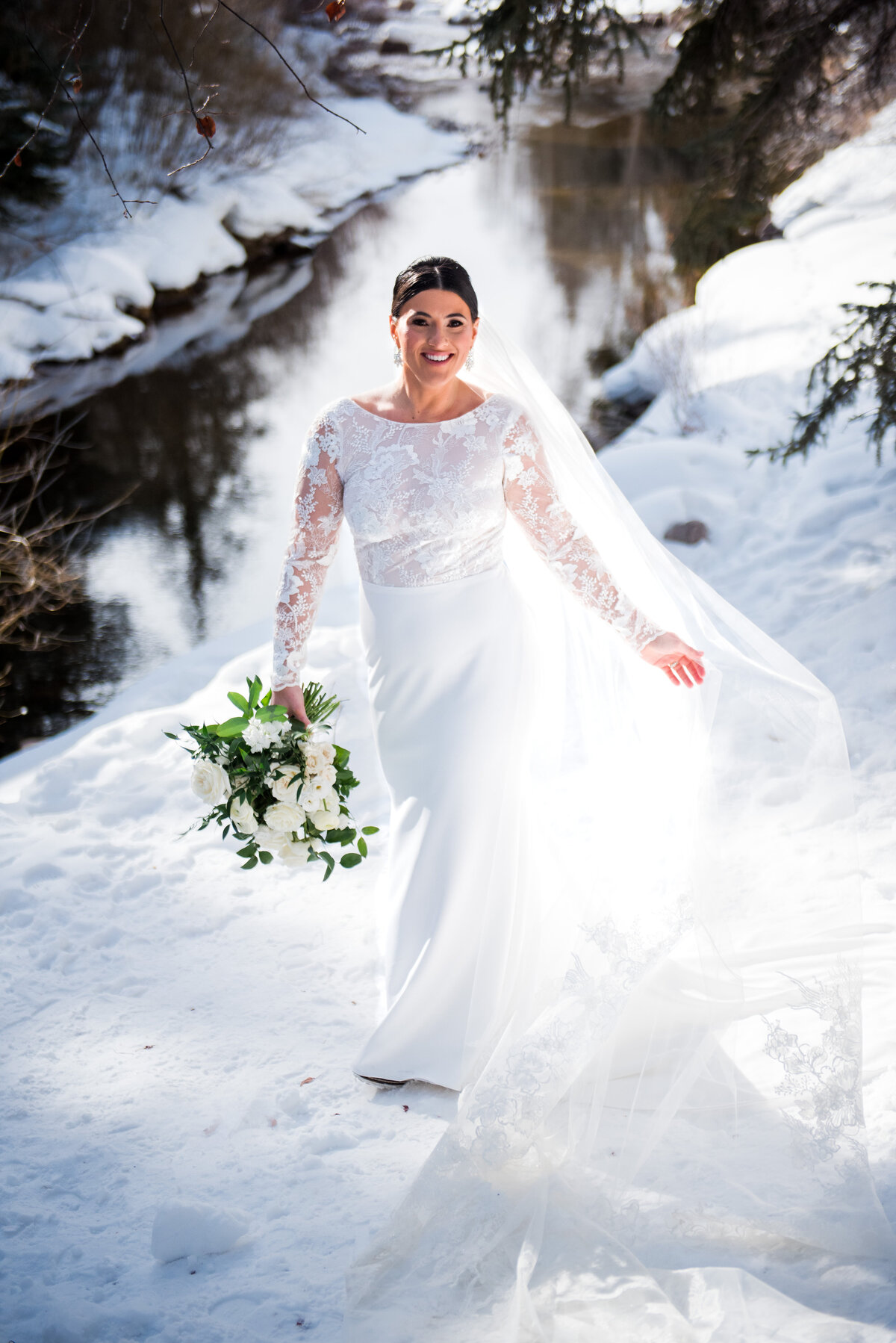 A bride smiles at the camera and playfully twirls her veil in snowy Vail, Colorado.