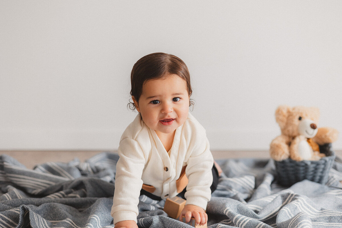 A baby boy sits on a blanket.
