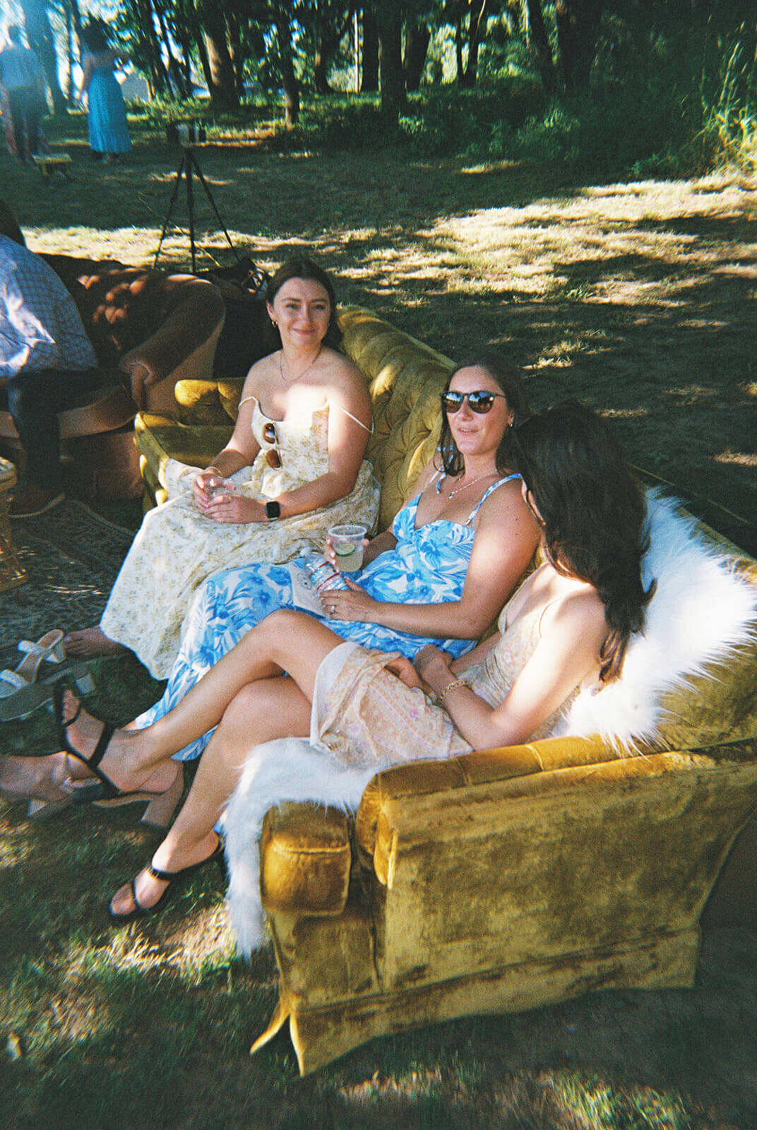 Three women sitting on a yellow couch outdoors.