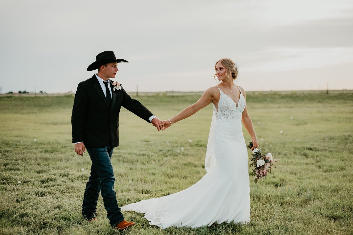 bride and groom walking and holding hands in field, texas panhandle wedding photography
