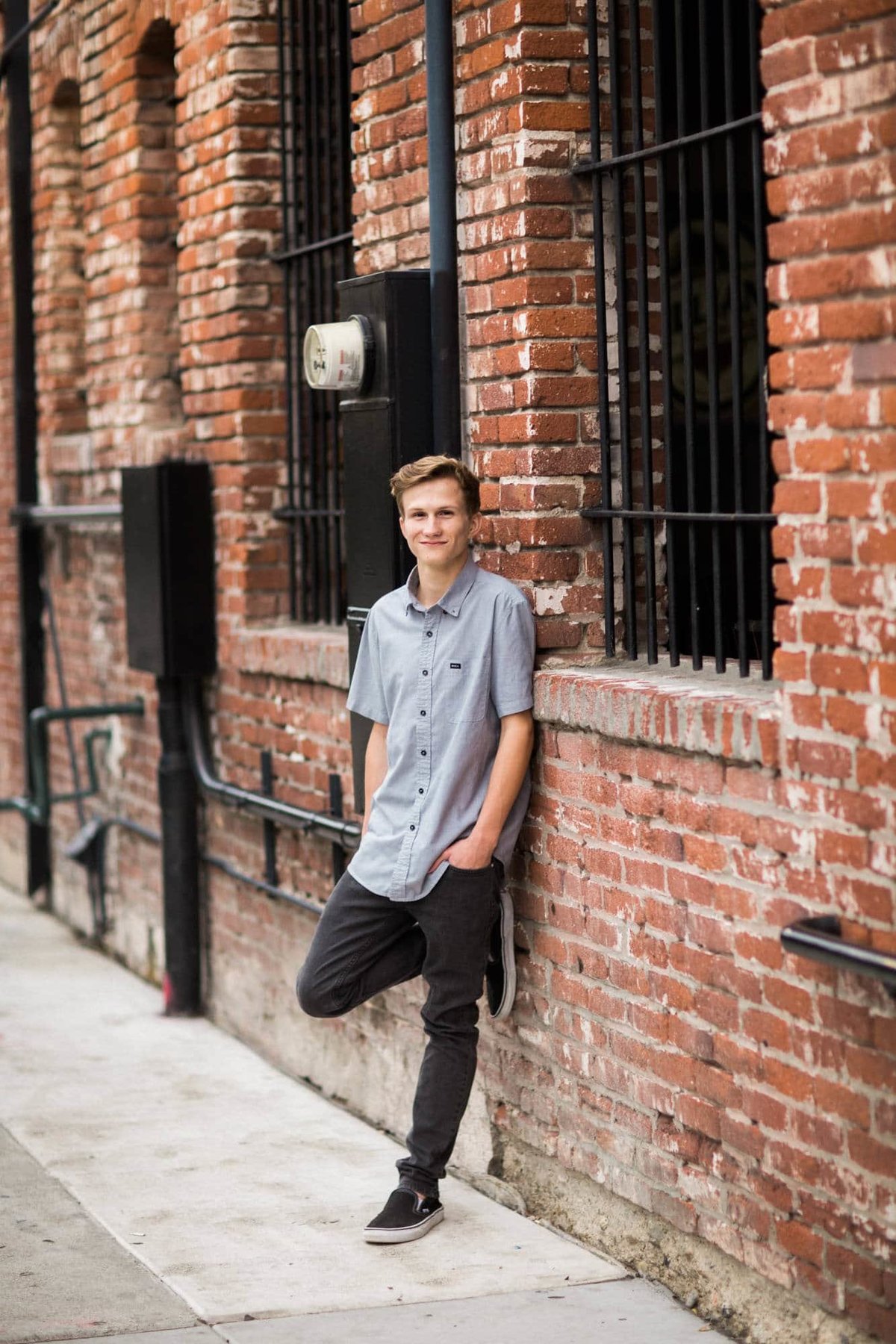 Young man leans against a brick wall during his senior photo session