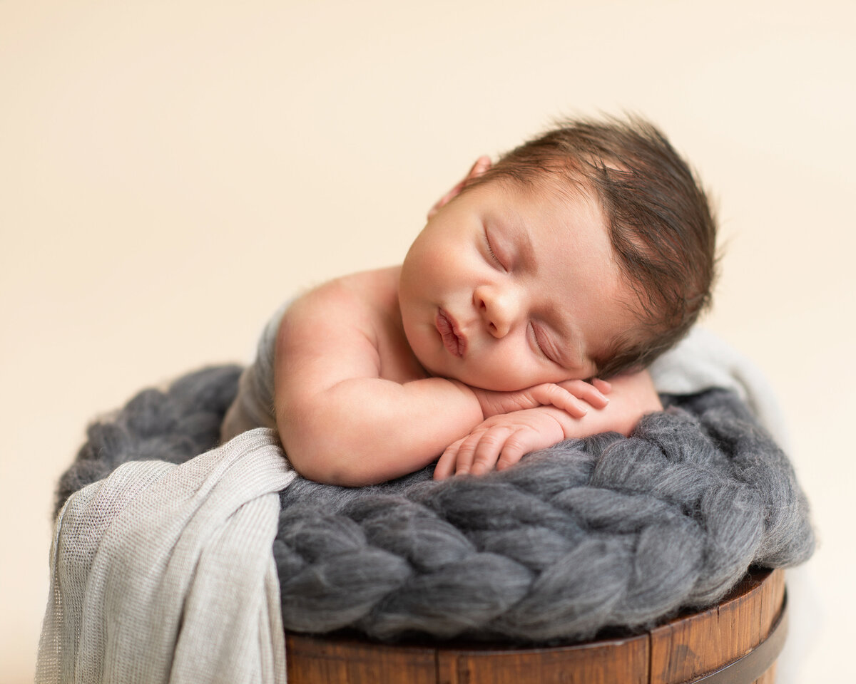 Newborn baby rests its head on the bucket with Adair Photography