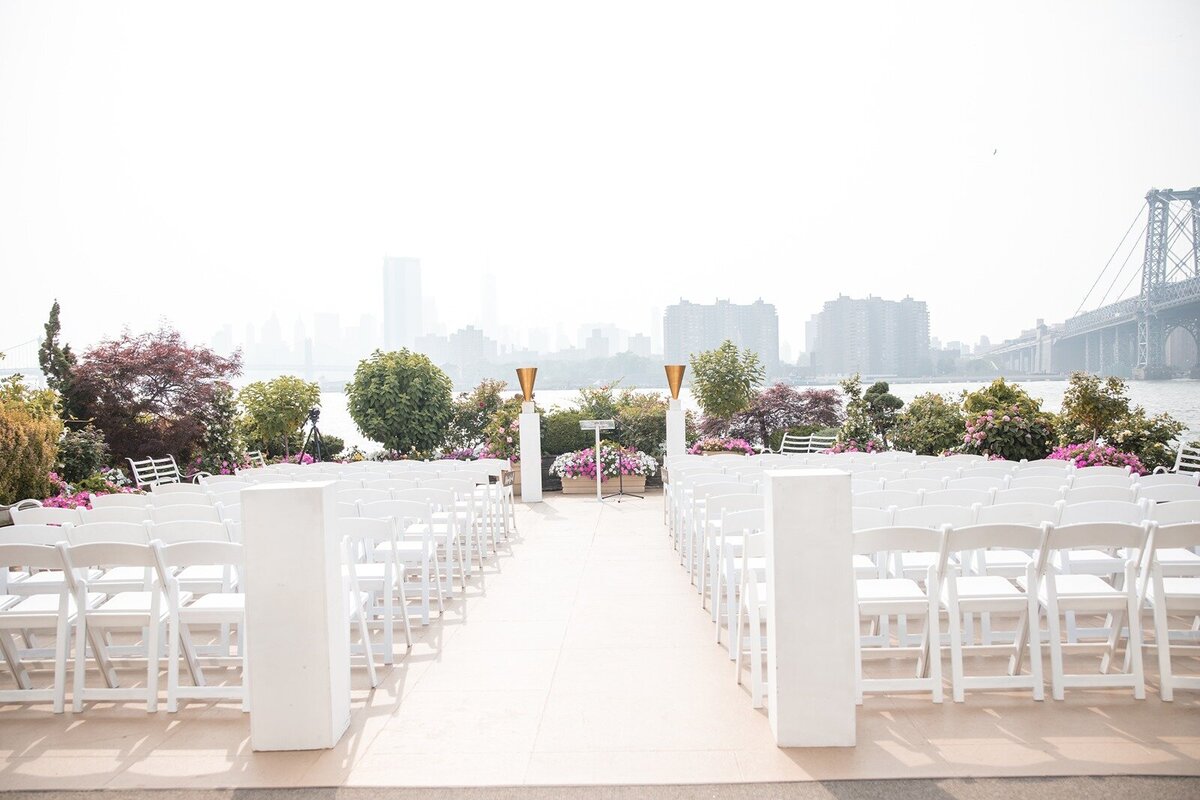 Wide shot of Giando's ceremony site set with white folding chairs and it's garden on the East River.