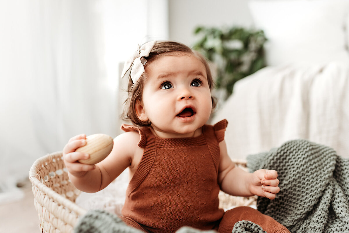 baby girl sitting in bassinet with egg shaker toy looking up