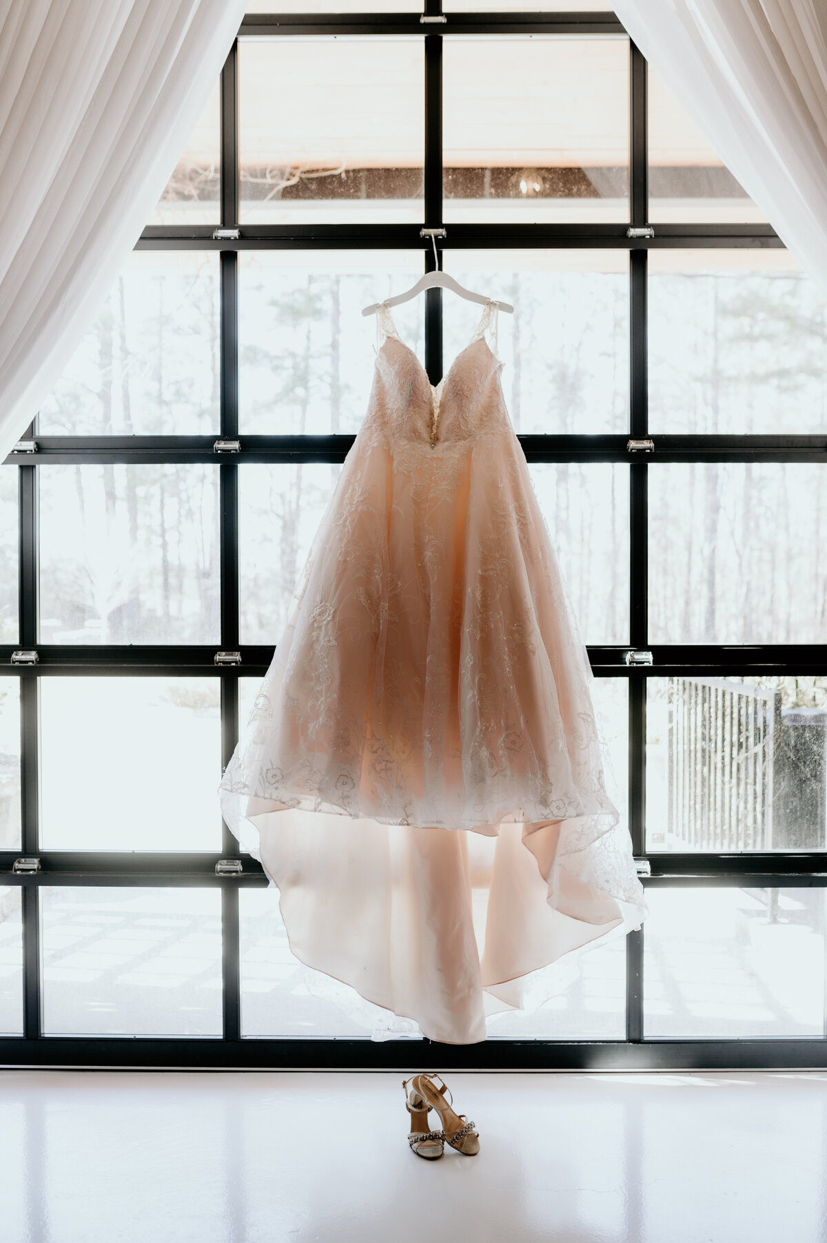 tulle and lace wedding dress hanging in the window of the little rock ar wedding venue with the brides wedding heels sitting under the dress