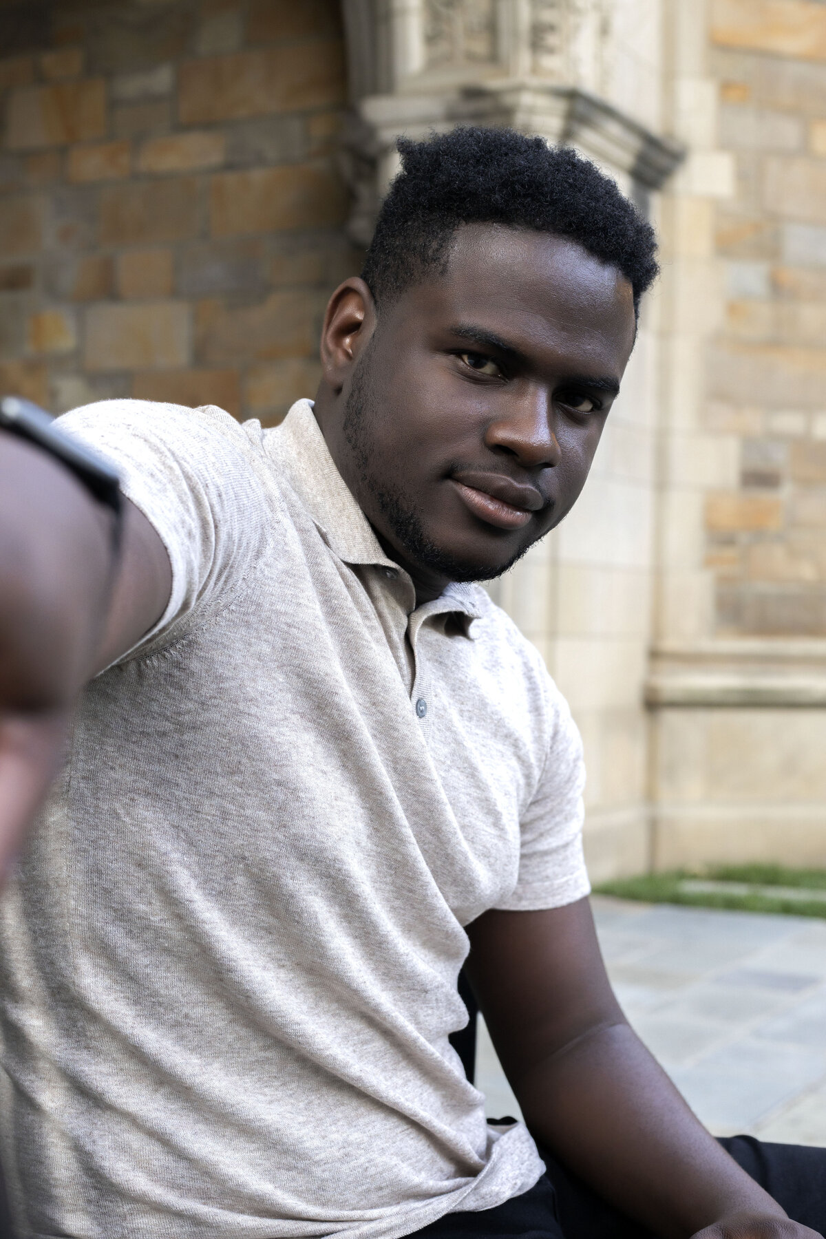 African American male wearing tan polo shirt and black jeans sitting on a bench