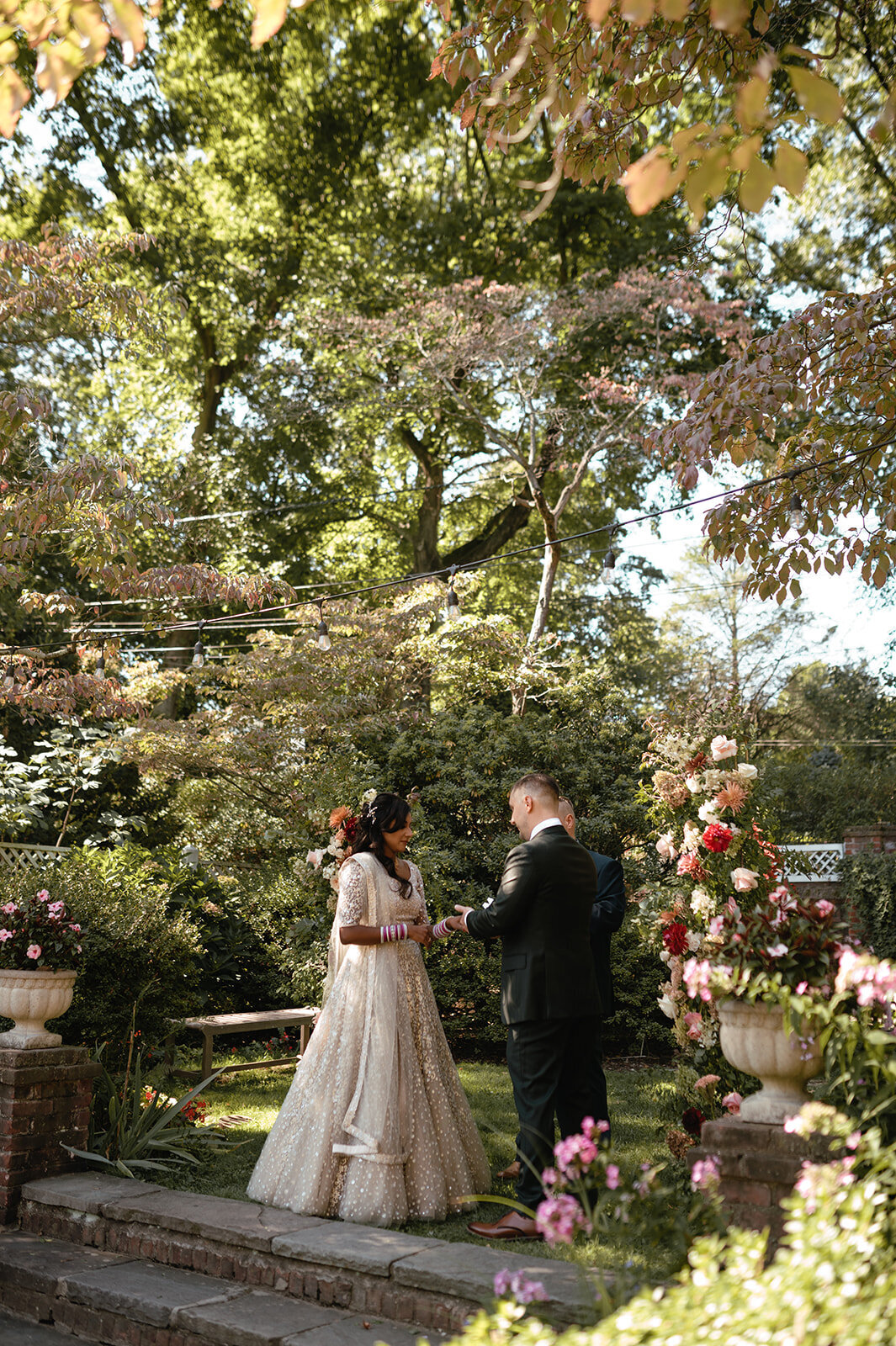 The couple standing before a floral arch, framed by a charming backyard garden and soft natural light.