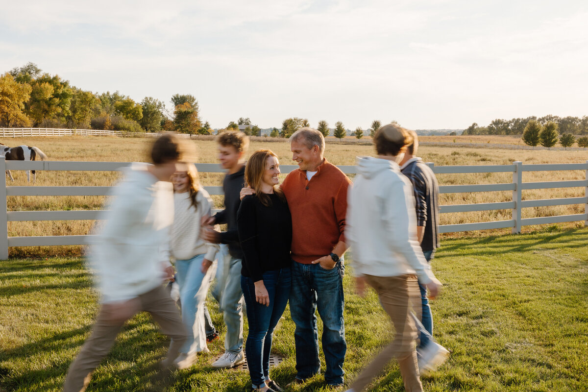 Kids running around their parents as they stand in a field