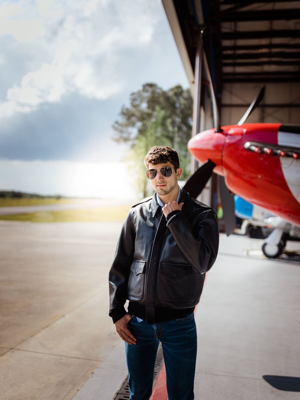 Senior portraits for this future pilot was at a a hanger with his favorite airplane in the background while he stands cool with his leather jacket and aviator glasses.