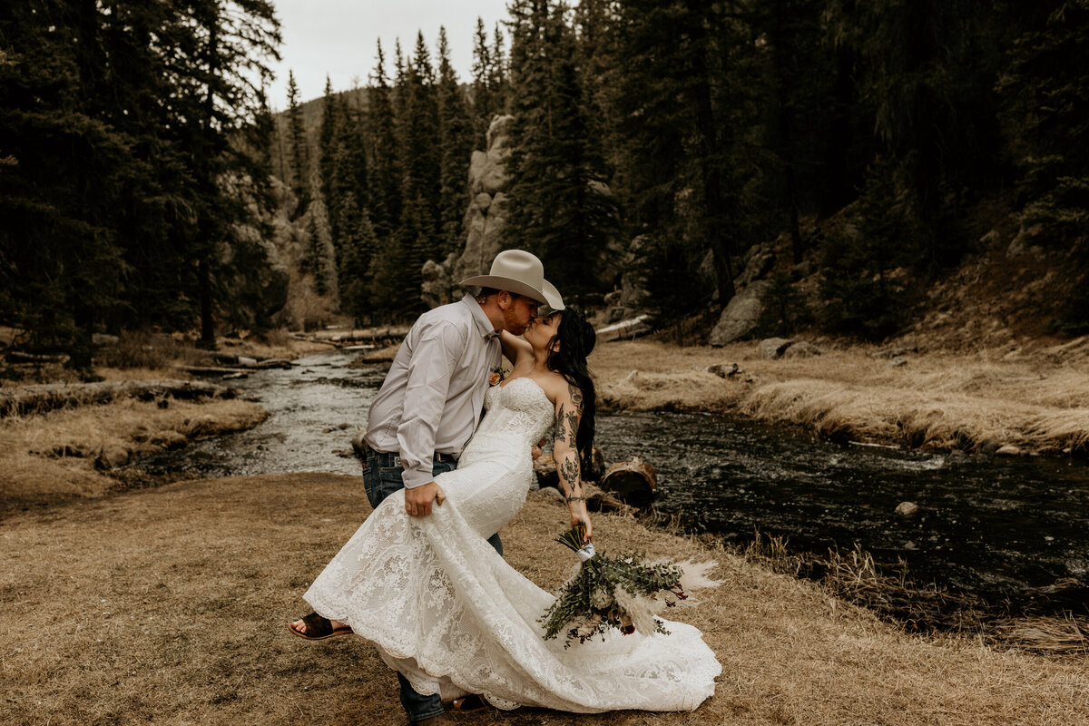 groom dipping and kissing bride in front of a Jemez Springs creek