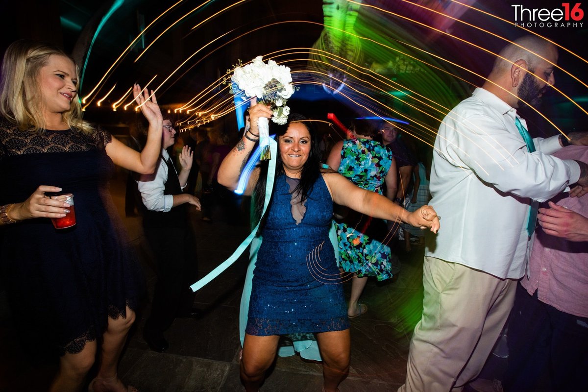 Female guest dances on dancefloor with bouquet she caught