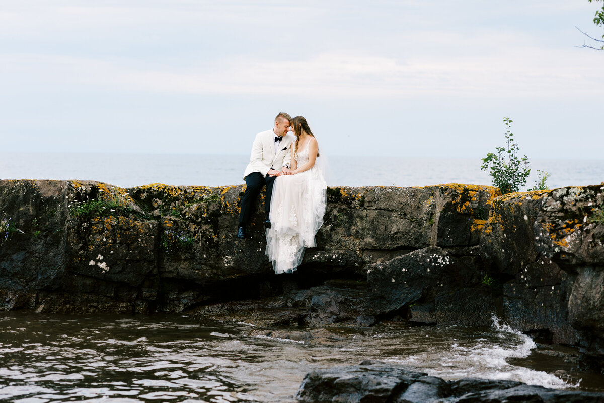 Bride and groom sitting and kissing on the rock at North Shore, MN