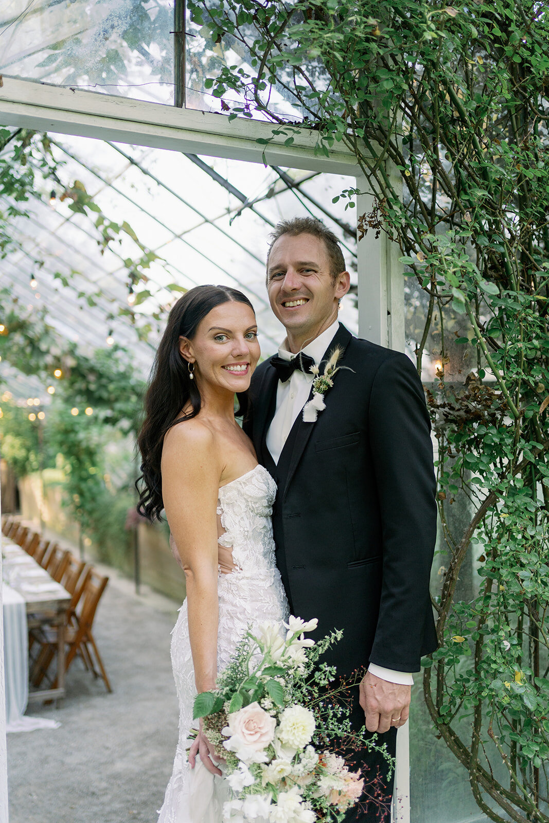 Couple standing together inside the greenery-filled Glasshouse Community greenhouse on their wedding day in Ottawa County, Michigan.