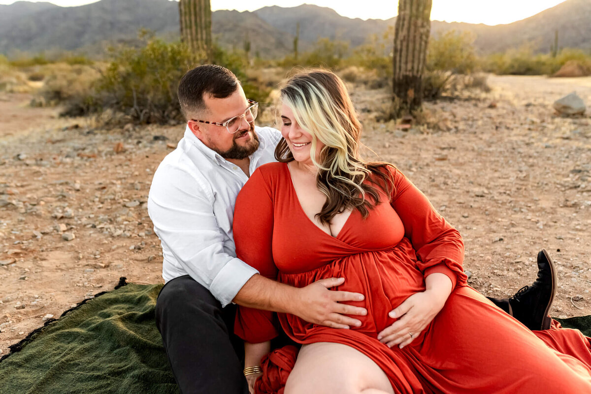 Expecting parents cuddle up close on a picnic blanket in the Arizona desert. Photo by Cactus & Pine Photography
