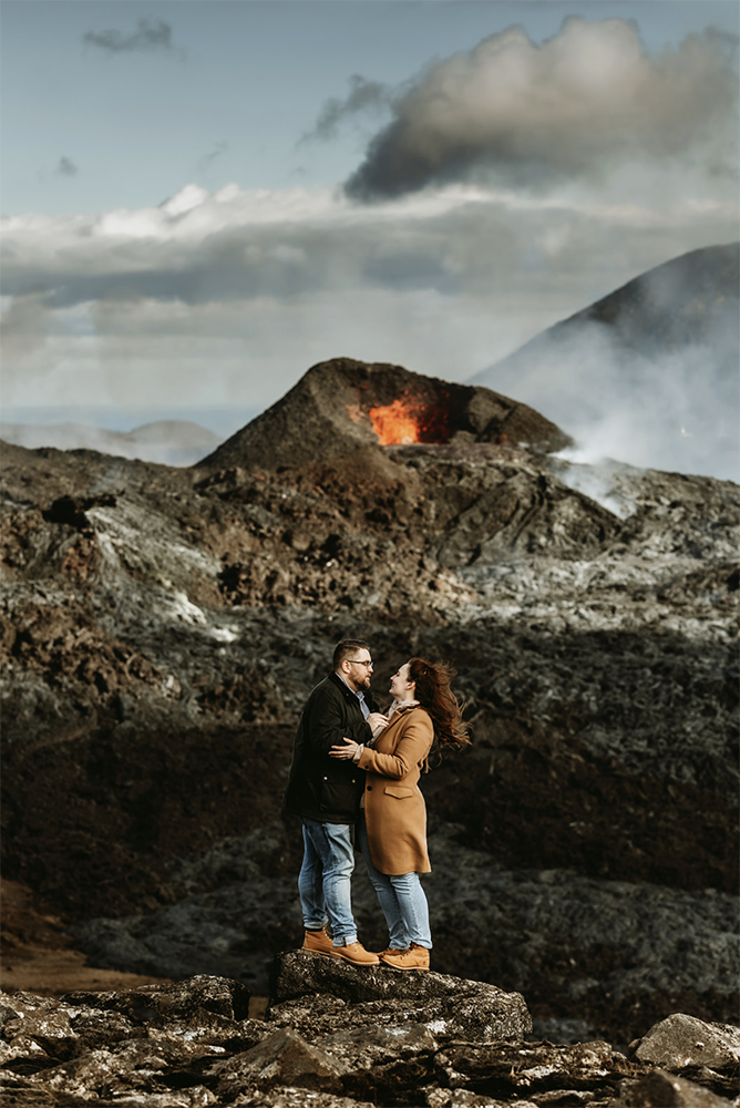 engaged couple is posing in front of an erupting volcano in Iceland