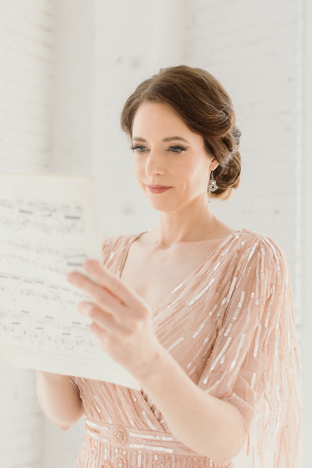 light skinned woman is light pink sparkly gown is reading music sheets. Photo is close up.