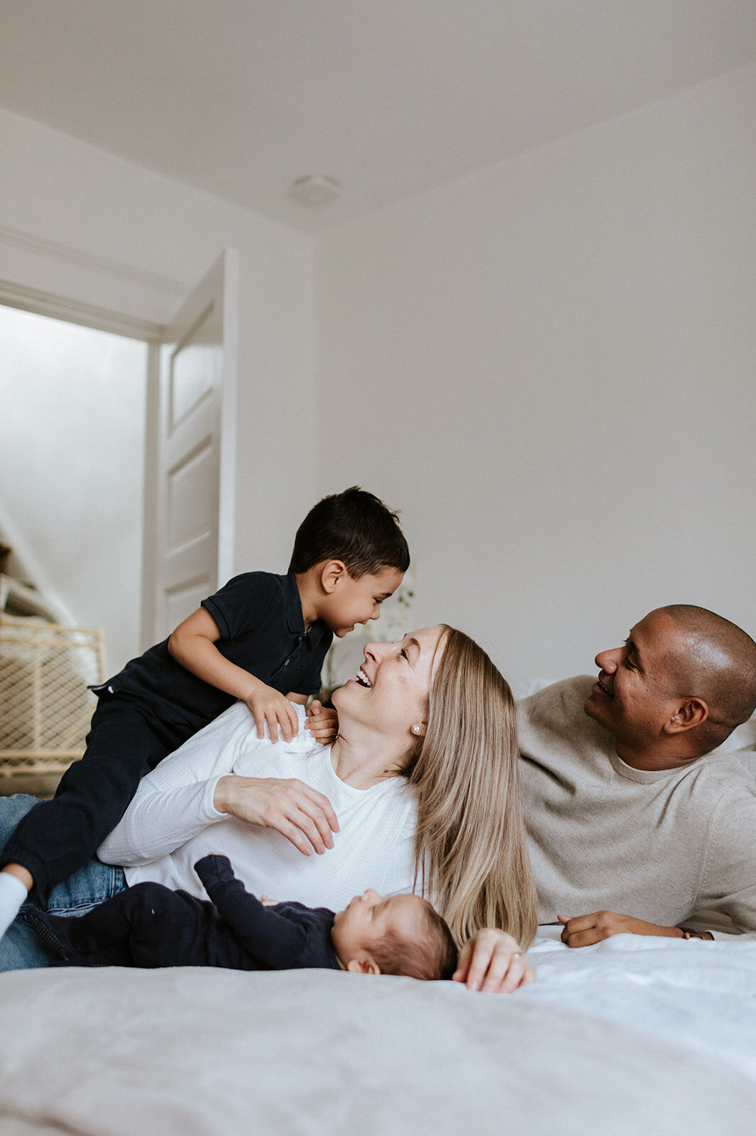 Captured by a talented Toronto family photographer, this intimate moment features a family of four on a bed: a woman gently holding a toddler, while the man relaxes nearby and the baby rests peacefully on her lap.