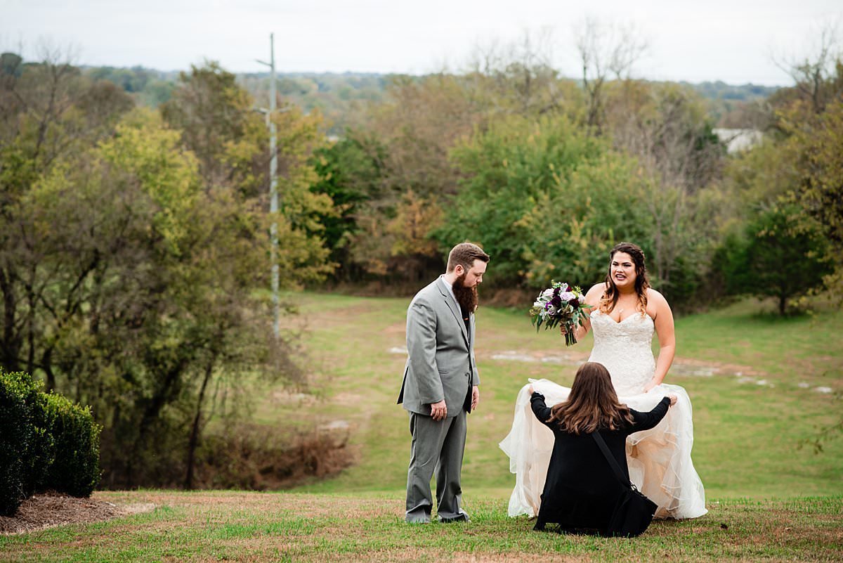 Photographer adjusting brides wedding dress during portraits on a hillside at The Pick Inn in Gallatin Tennessee