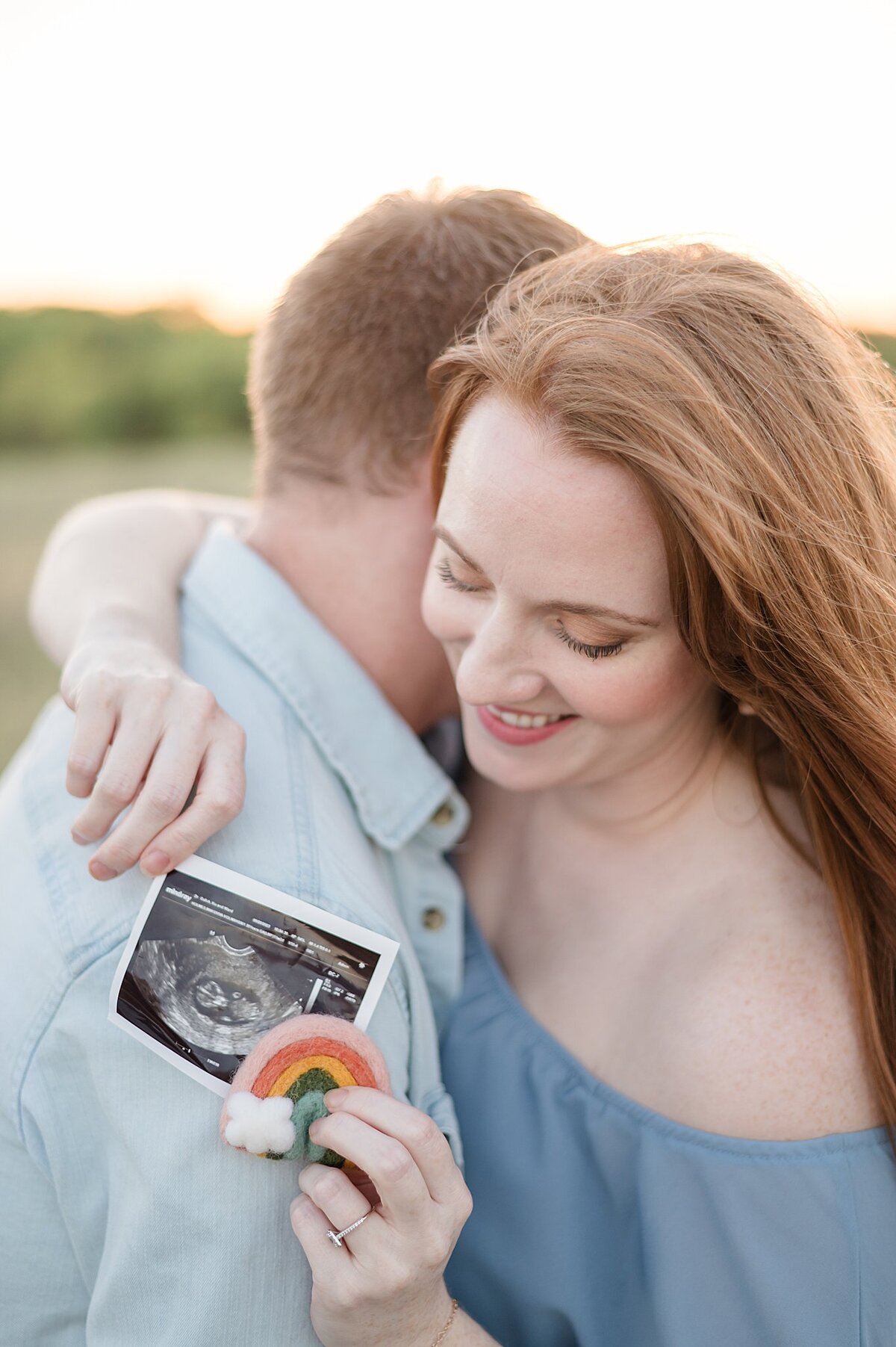 husband and wife holding  ultrasound picture of their rainbow baby