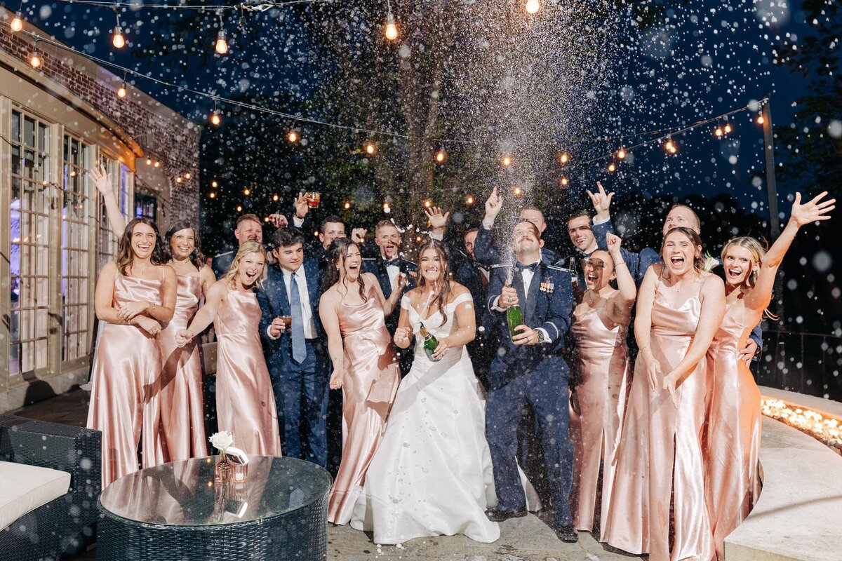 A wedding celebration with the bride, groom, and guests cheering during a festive confetti toss at night.