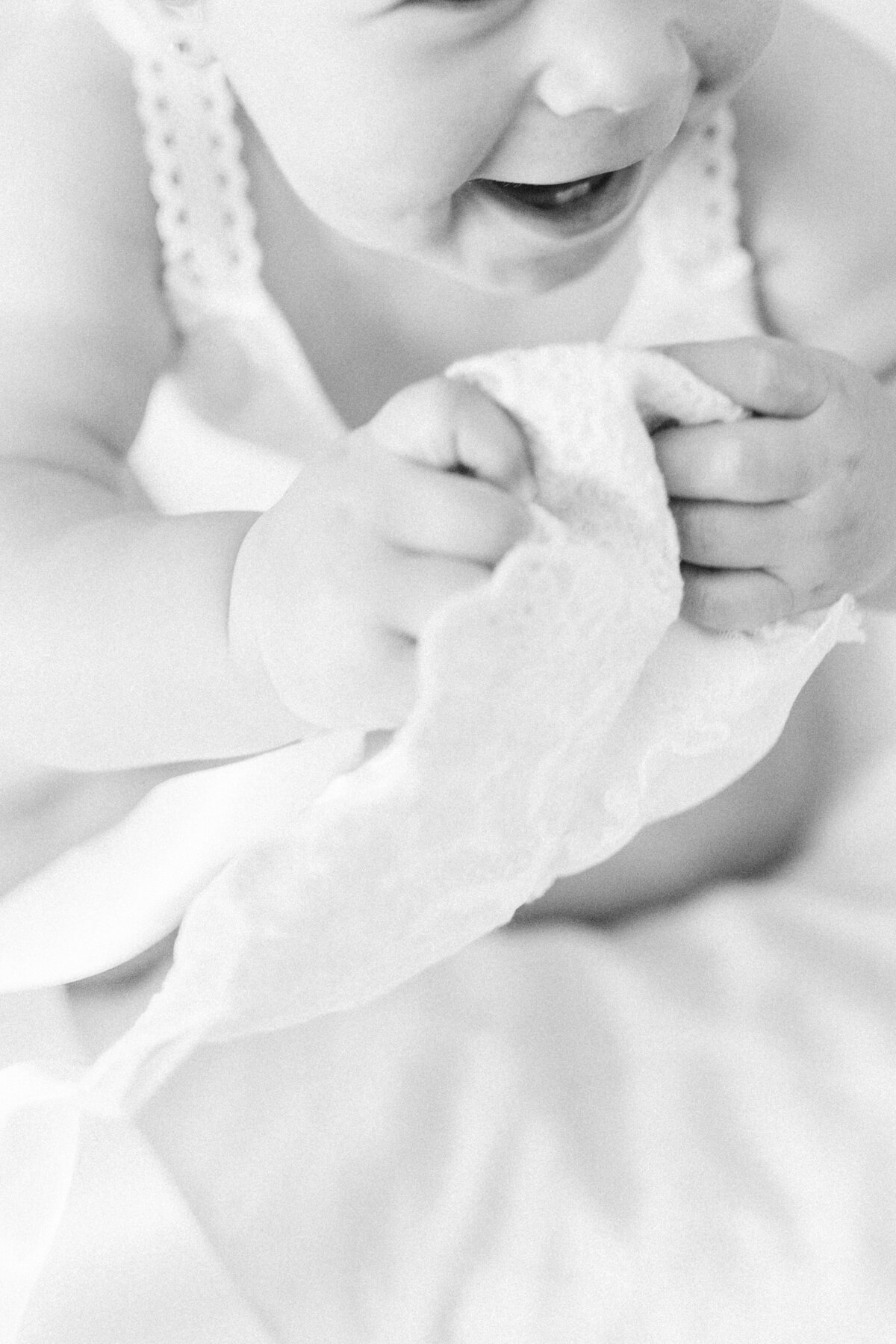 Timeless black-and-white image capturing baby’s hands wrapped around a baptism bonnet’s edge.
