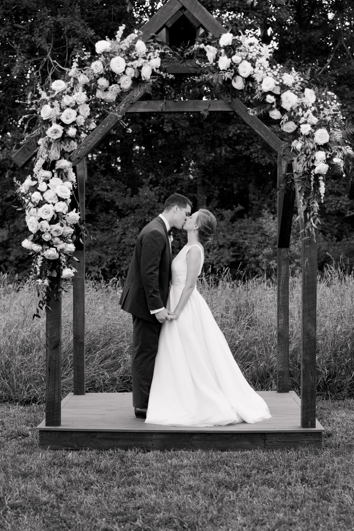 Bride and groom kissing underneath a wooden arch decorated with flowers