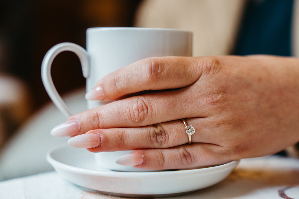 Hand holding teacup showing engagement ring
