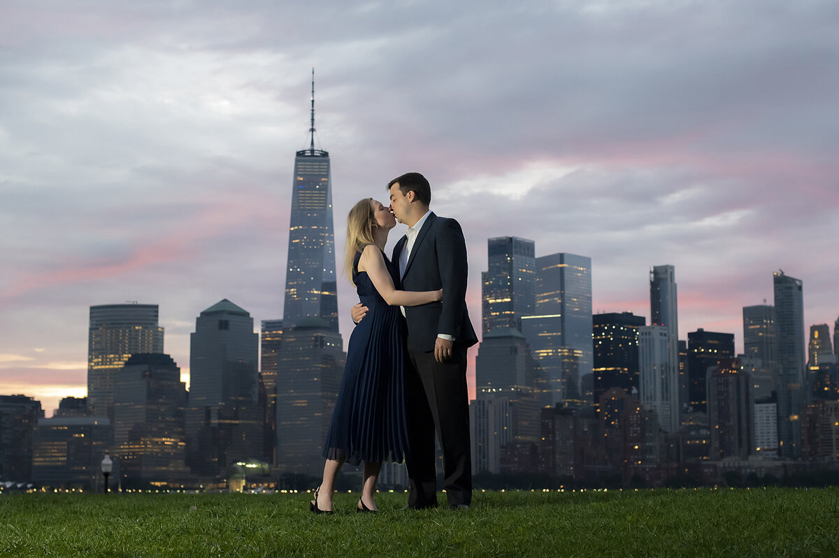 A couple with their arms around each other kissing with a city skyline behind them 