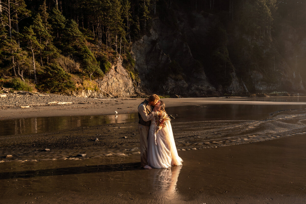 During their Oregon coast elopement, a couple kisses on the beach during a hazy golden hour