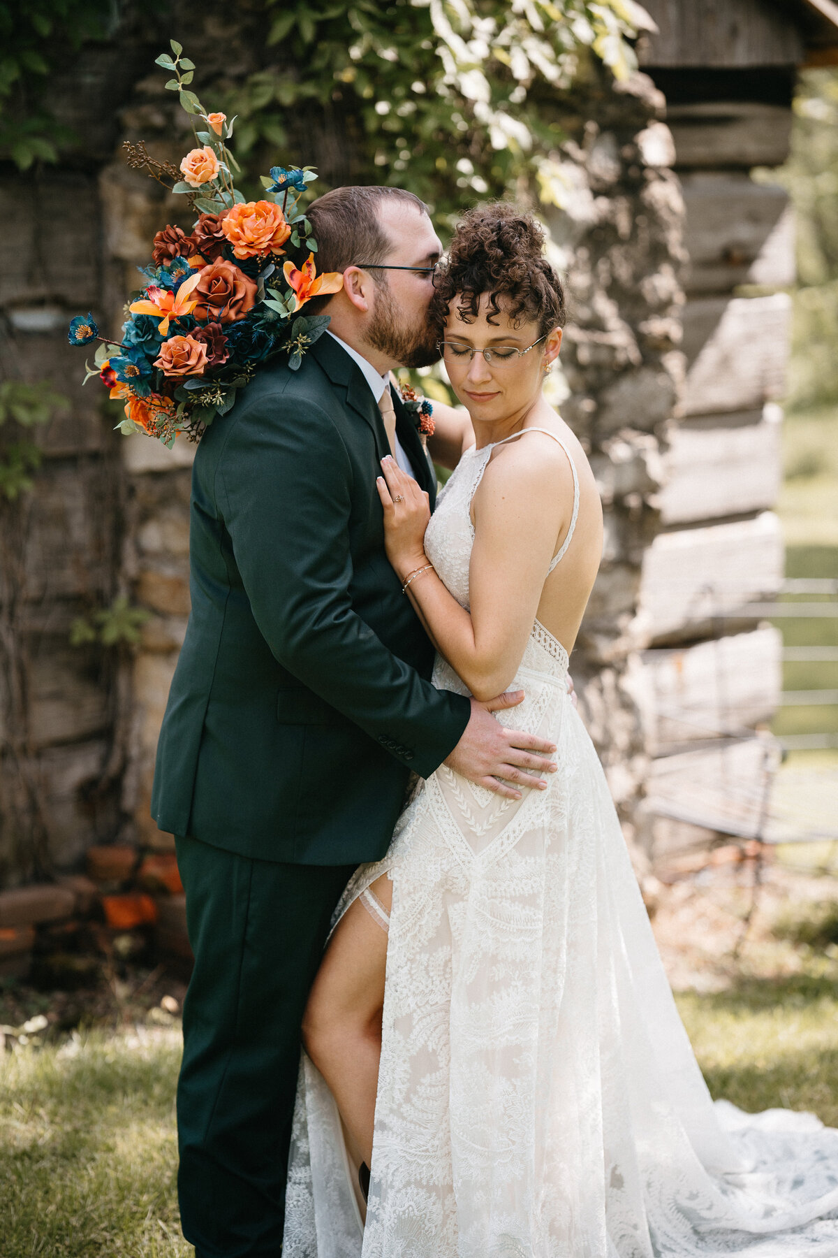 Groom kisses the side of brides head while he embraces her