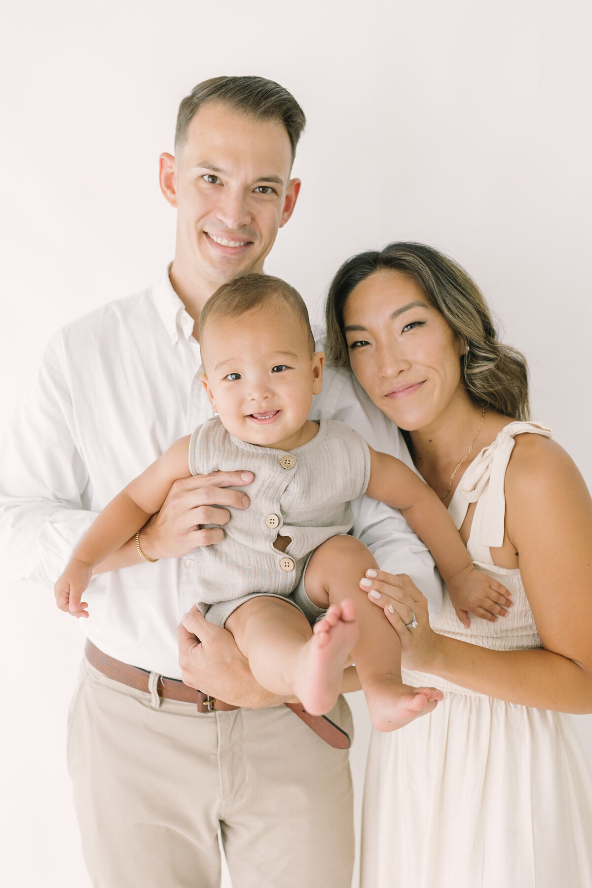 A joyful mom and dad holding their baby boy during a bright studio session in neutral tones — Raleigh portrait photos.