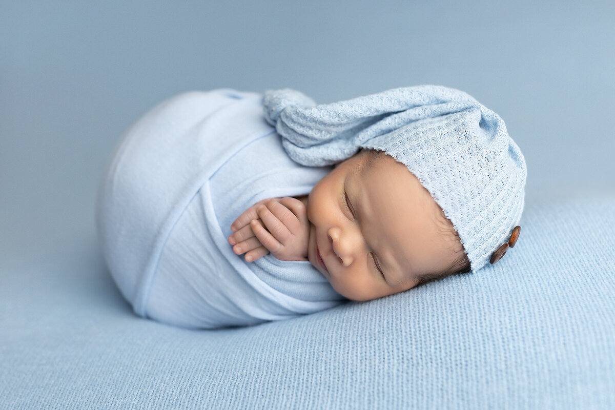 Newborn in soft blue wrap and knit bonnet, sleeping peacefully — newborn pictures by Dallas photographer.