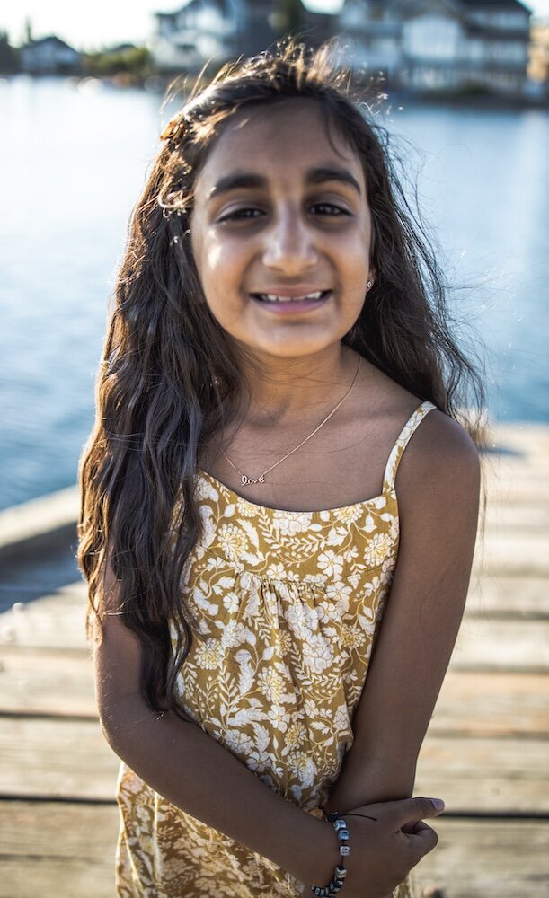 A little girl with long brown hair wearing a yellow floral dress