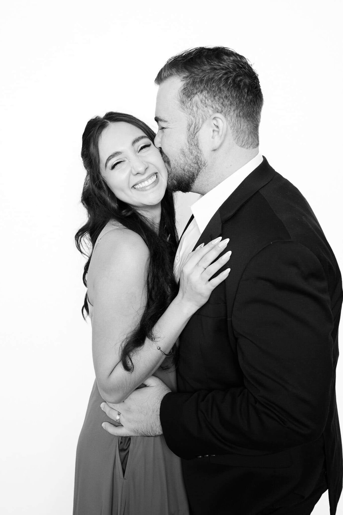A joyful couple sharing a kiss and laughing during a black and white portrait session with Monochrome Portraits, a modern photo booth experience in Phoenix.