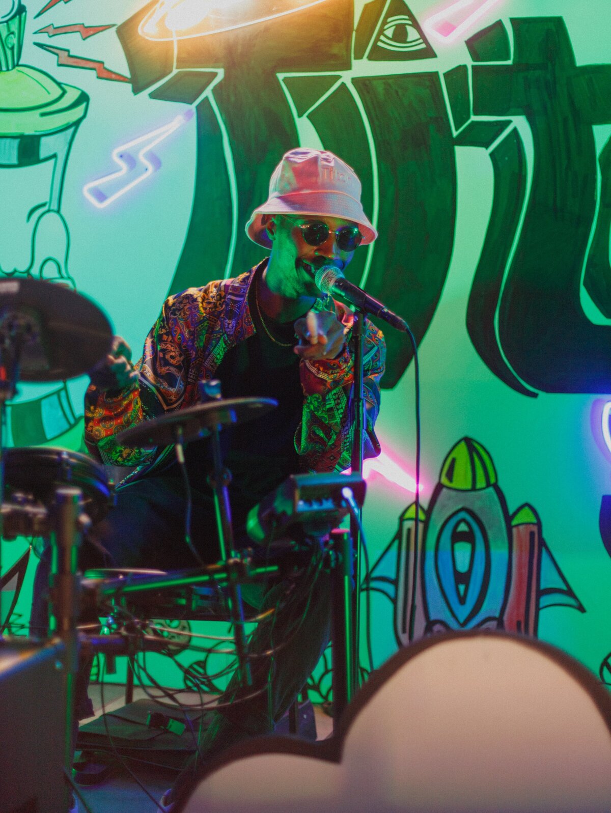 Musician performing under neon lights, set against a colorful mural backdrop.