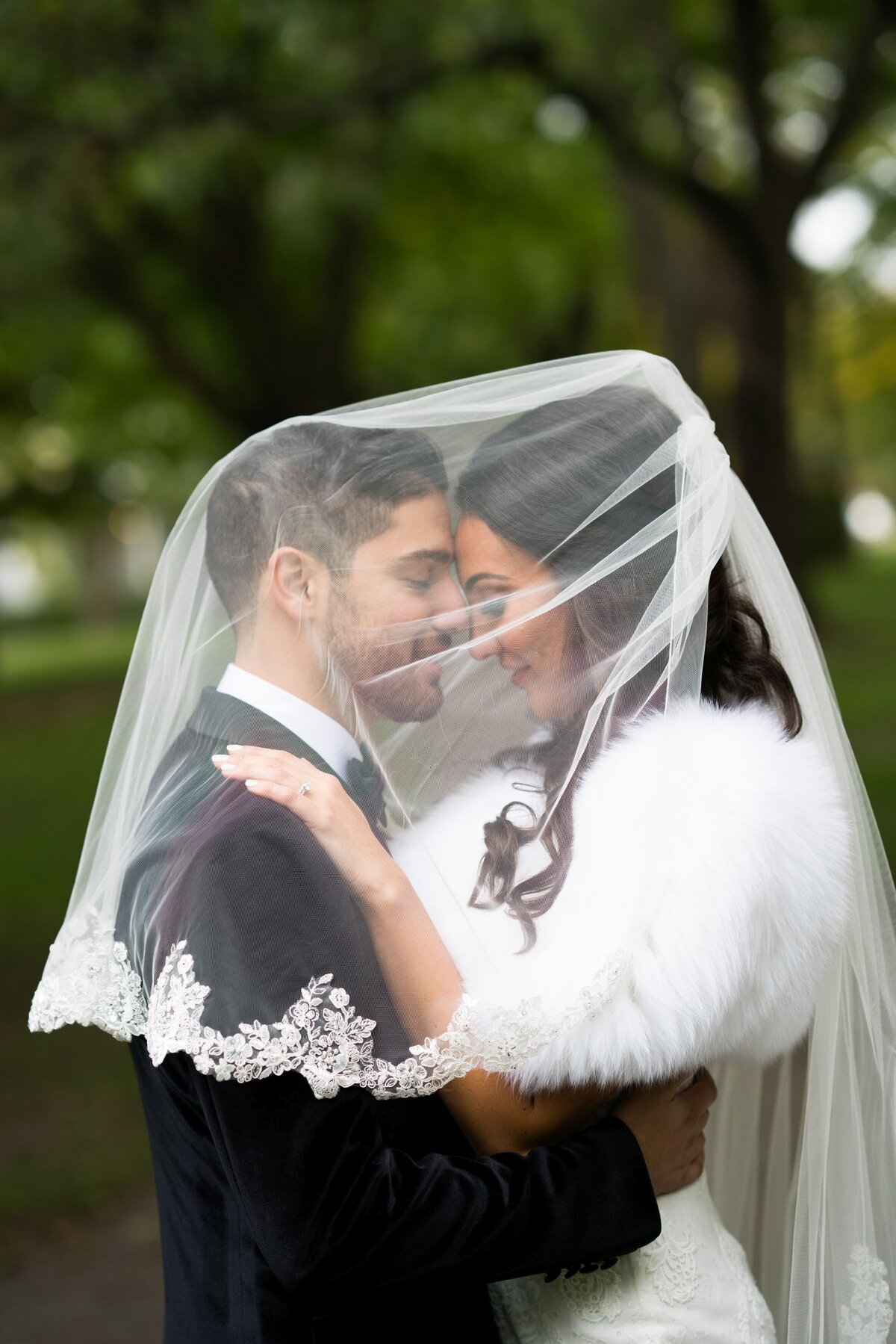 A romantic moment where the groom is under the bride's veil, with both smiling warmly at each other. The intimate setting highlights their connection, encapsulating the joy and love shared on their special day.