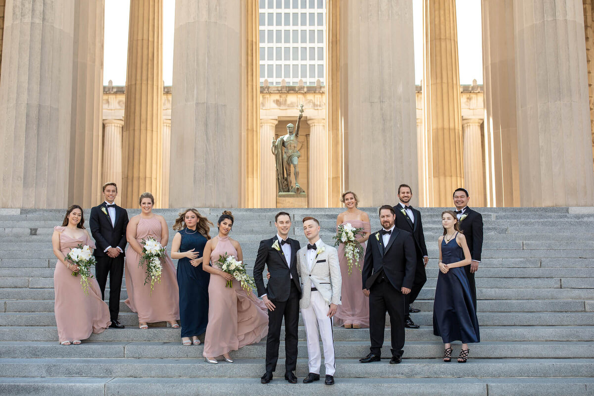 Two grooms with bridesmaids and groomsmen at War Memorial Plaza steps in Nashville, TN