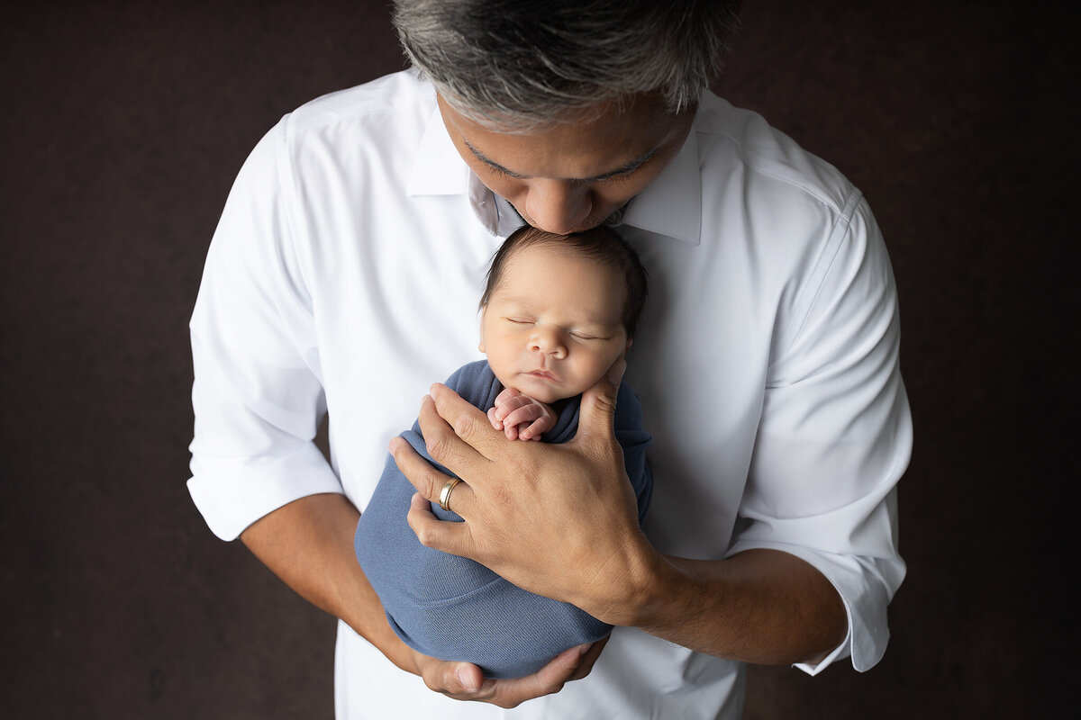 Baby held closely by father in white shirt, eyes closed — newborn photographer in Dallas.