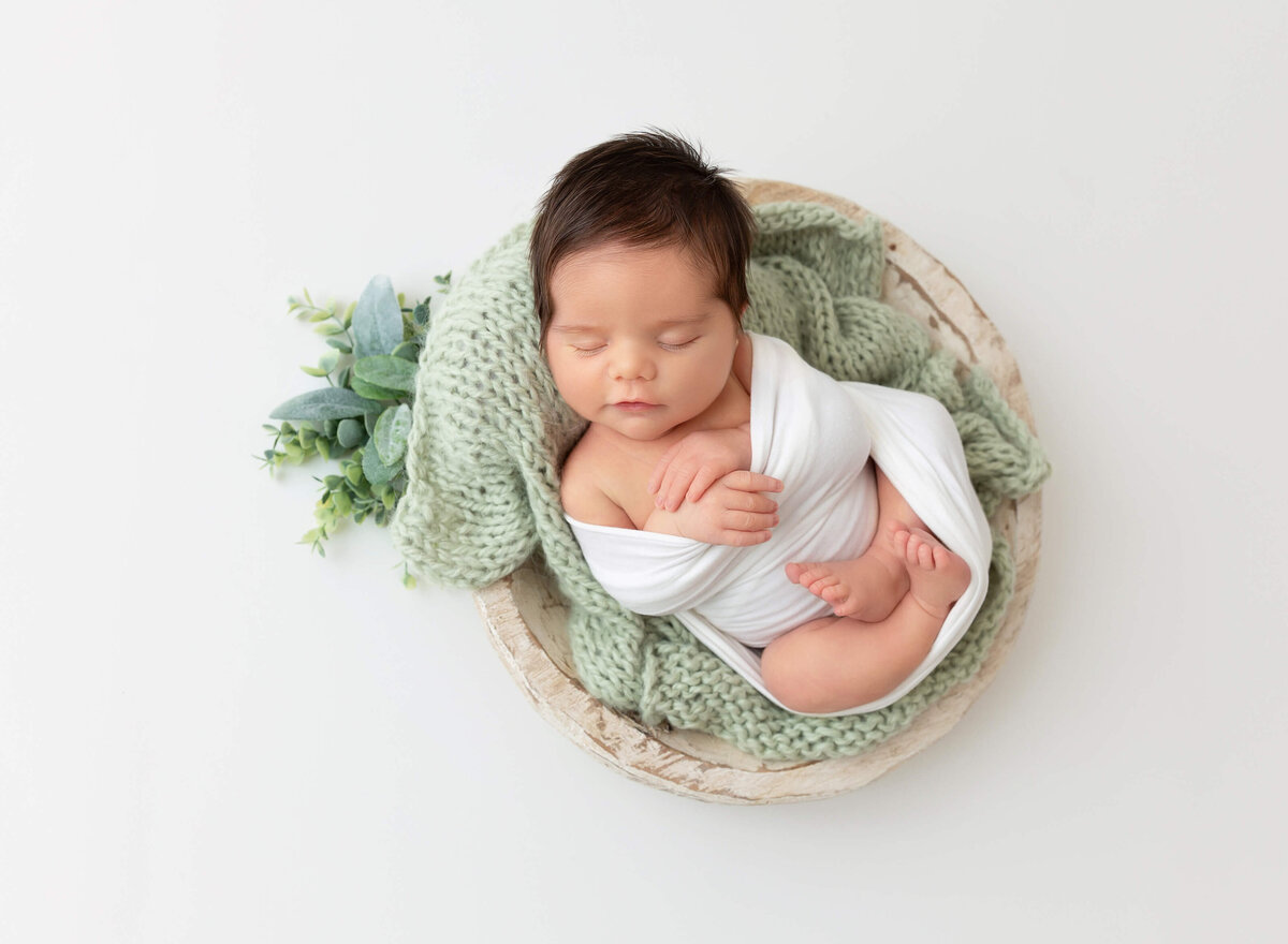A newborn boy curled up in a cozy pose, captured in an artistic baby photography session in New York City