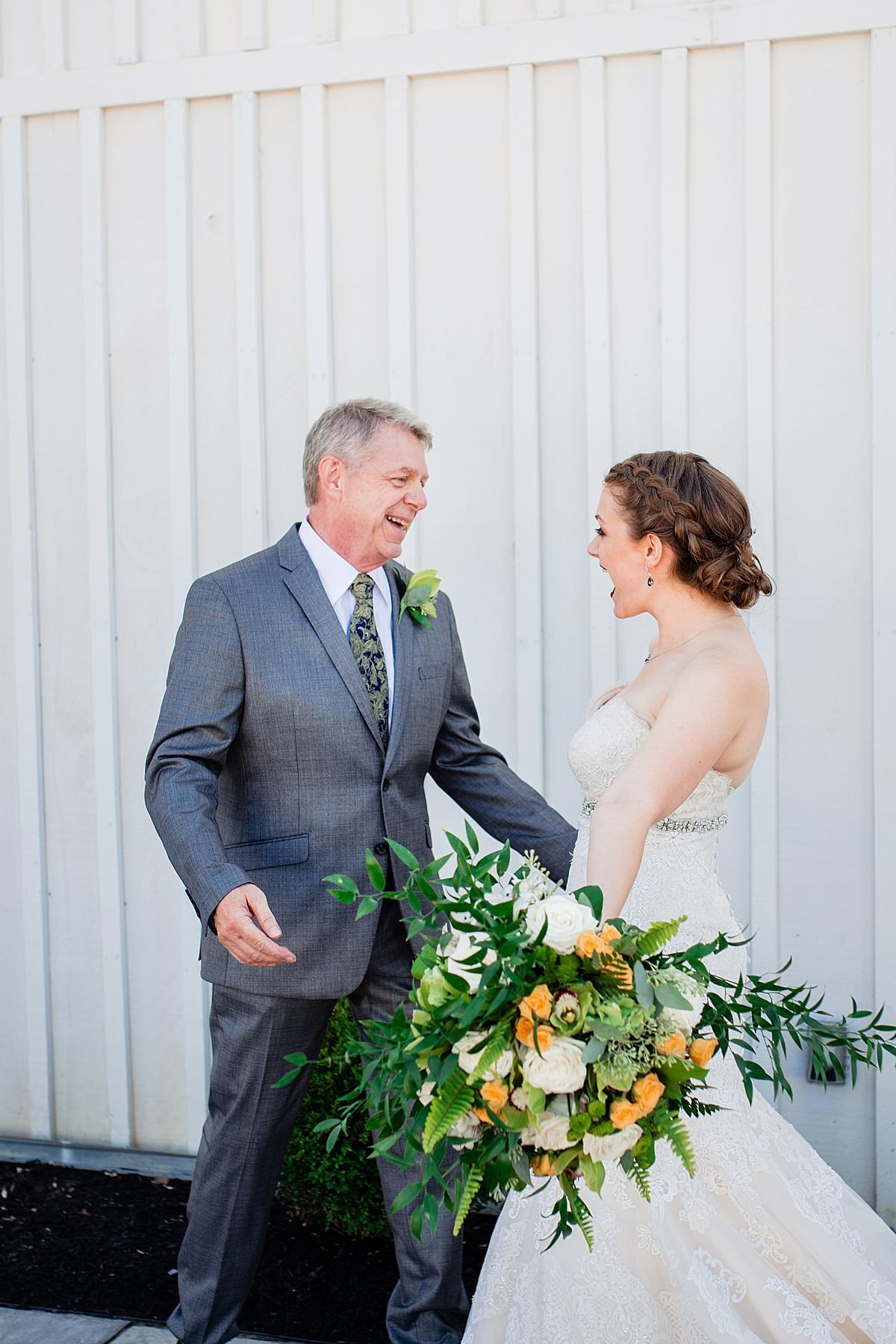 Father of the bride has first look with his daughter while she holds a yellow, orange and ivory bridal bouquet