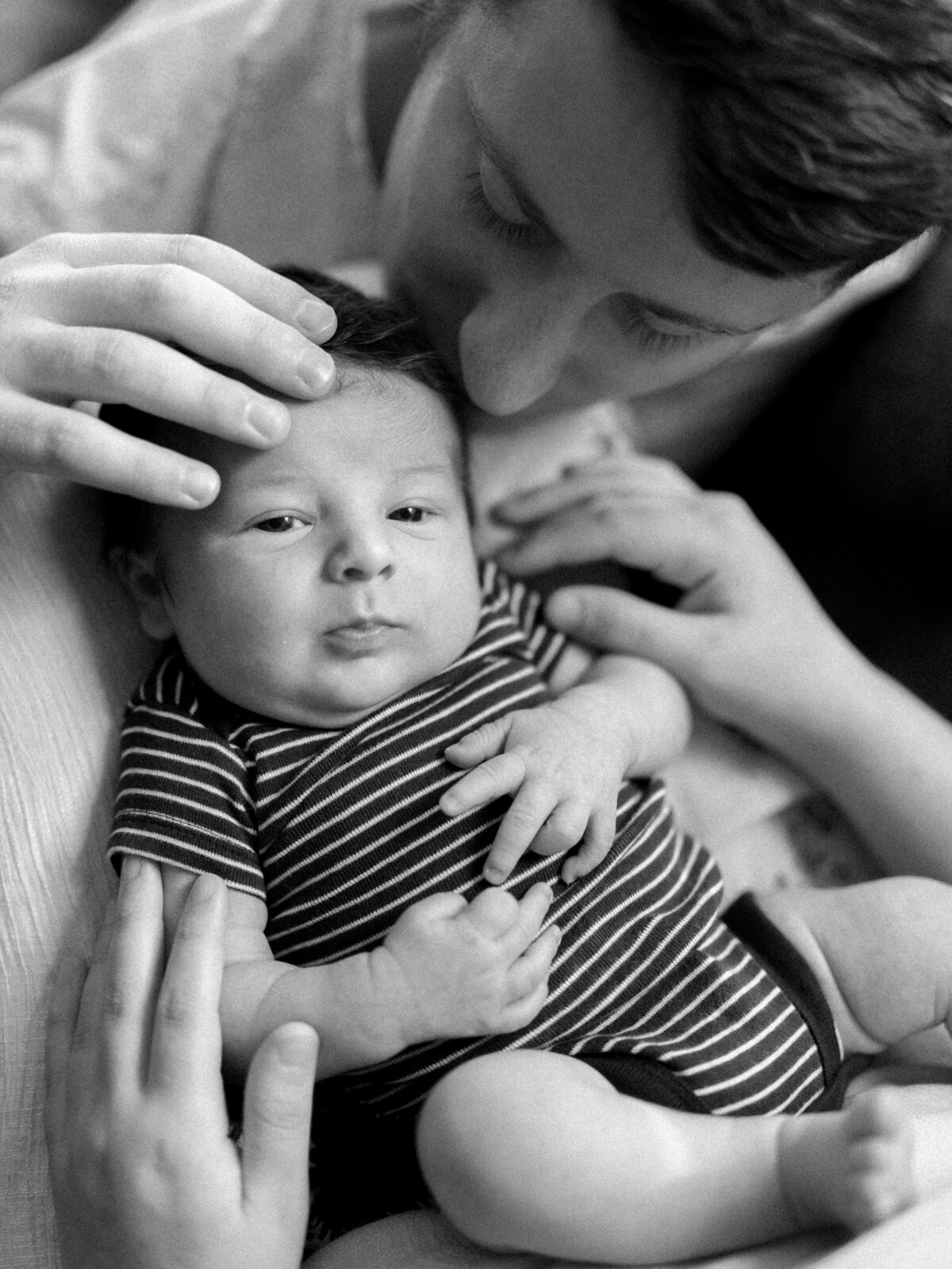 Black and white photo of a baby being kissed by his parents