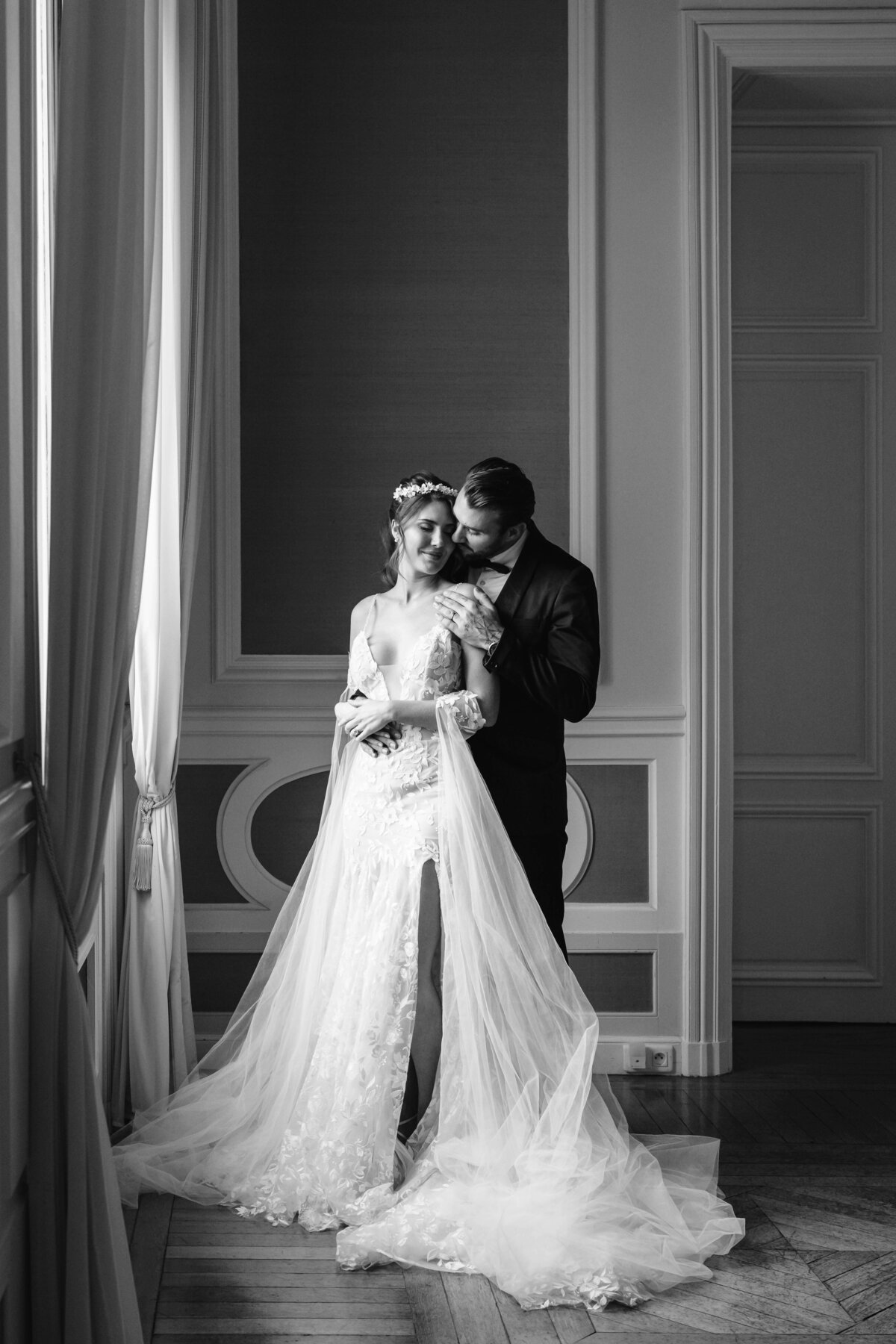 black and withe photo of a bride and a groom standing next to a window