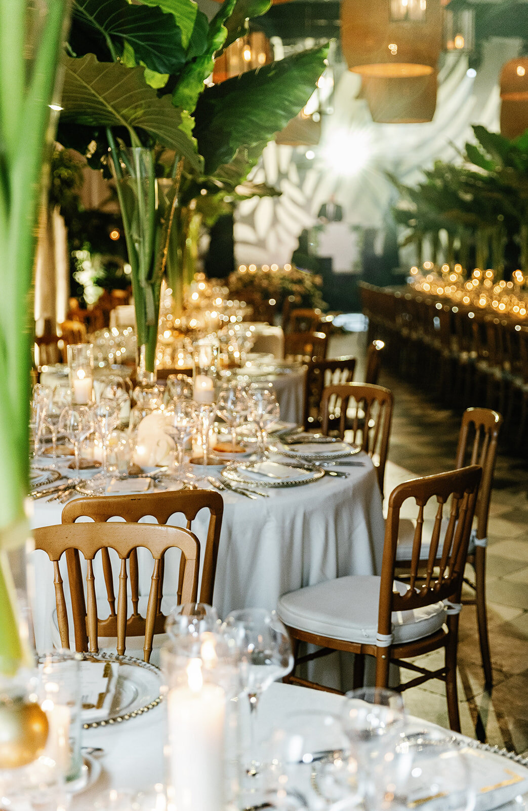 A luxurious wedding reception setup featuring candlelit tables, lush greenery, and elegant gold-accented decor.