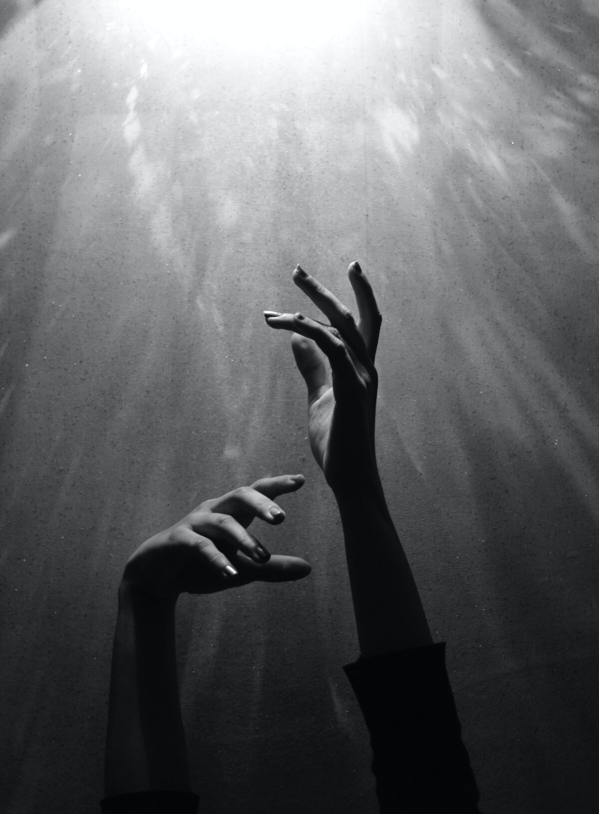 A black and white image of two hands reading up towards a white light.
