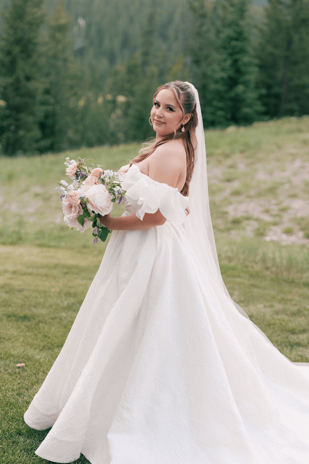 Bridal portrait at a summer wedding at Moonlight Basin, featuring a textured gown, flowing veil, and pastel bouquet with forest views in the background.