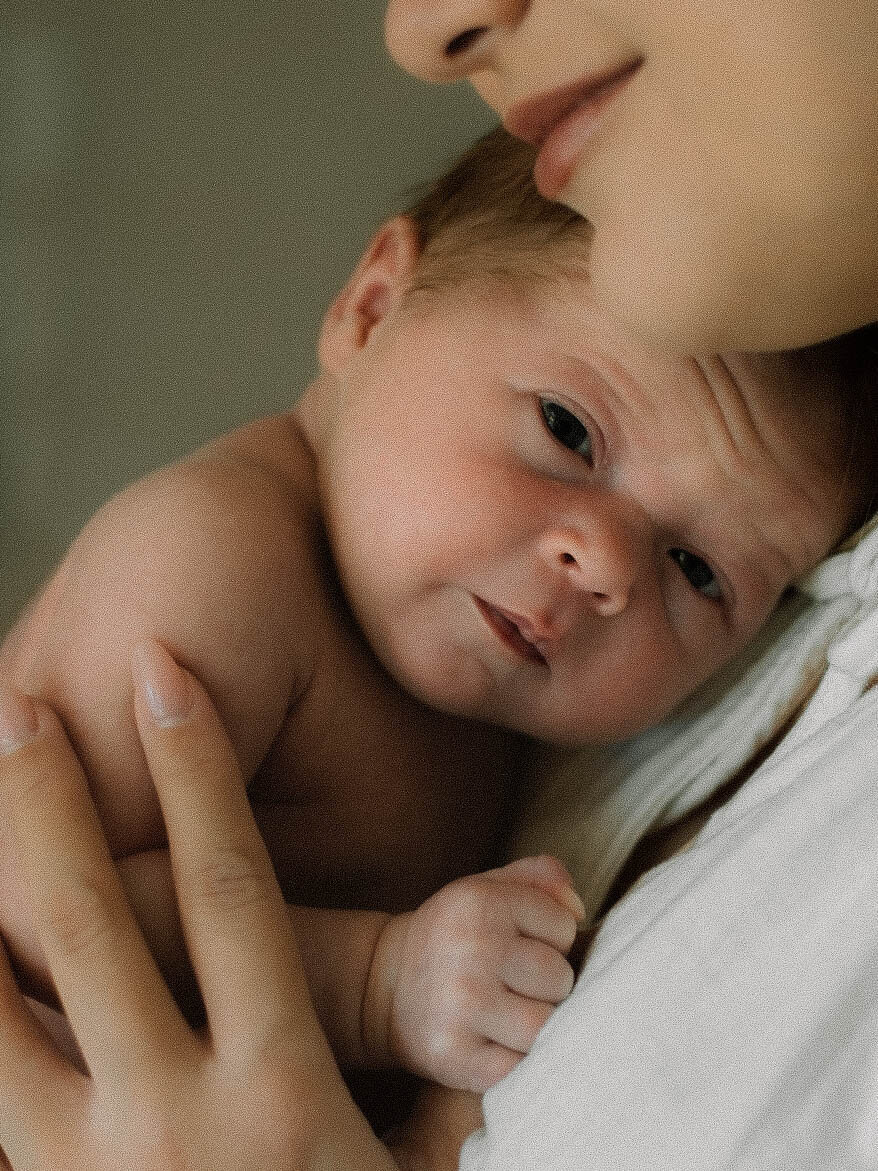 Baby resting on mom's chest while looking at the camera in a newborn session at home.