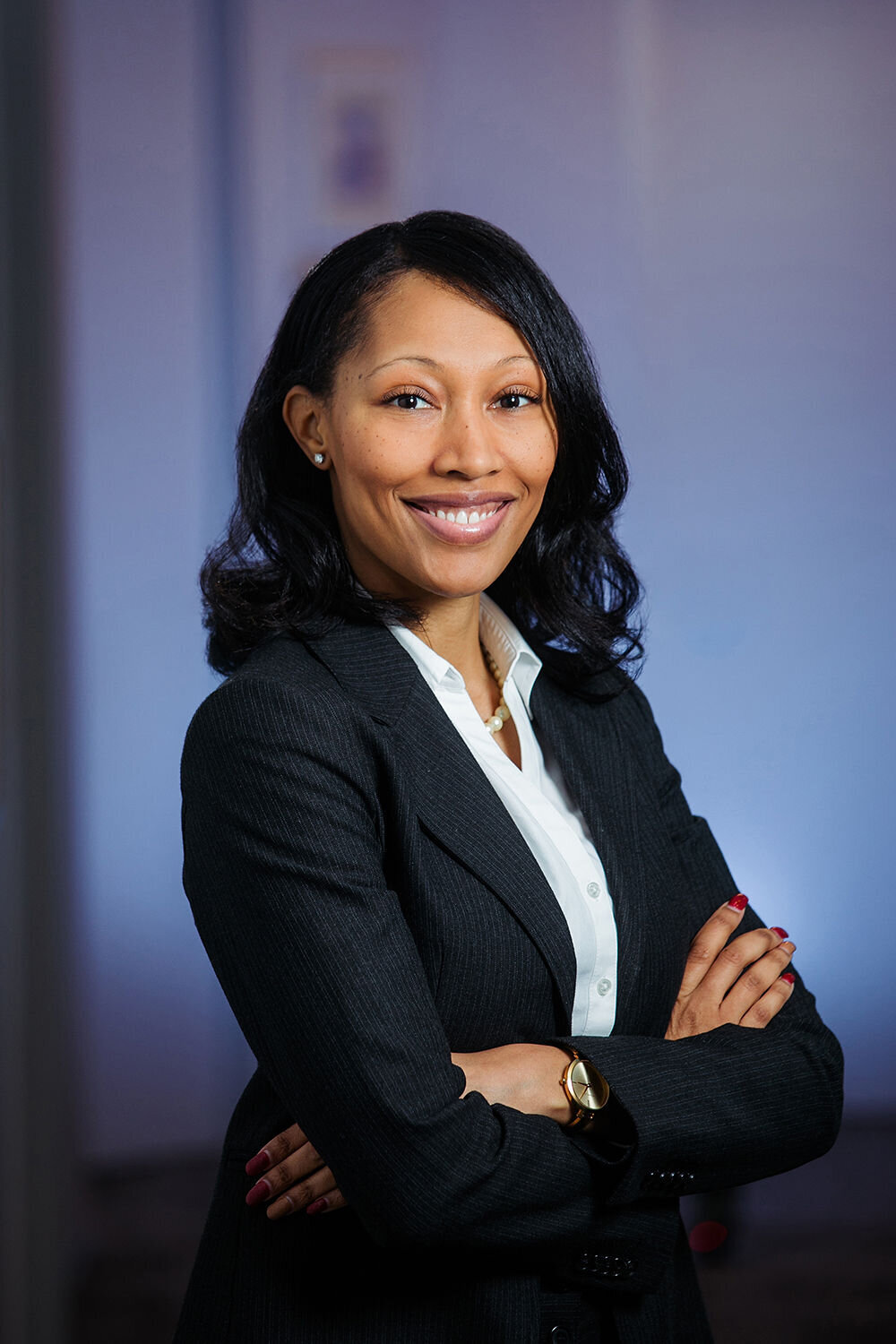 A woman stands with crossed arms, smiling, in a blazer.